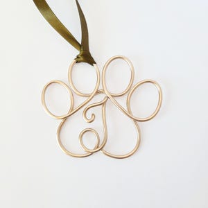 May include: A gold-colored wire paw print ornament with a green ribbon for hanging. The paw print is made of looped wire, creating a delicate and airy design. The ornament is likely for pet lovers.