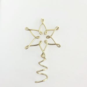 May include: A gold-colored, wire Christmas tree topper in the shape of a six-pointed star. The star has looped ends on each point. A spiral wire extends downward from the star.
