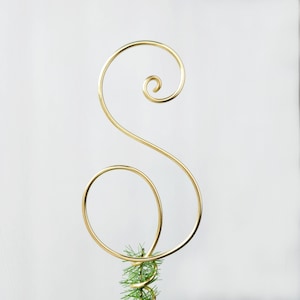 May include: Gold metal tree topper shaped like a stylized letter S. The topper is designed to be placed on top of a Christmas tree.