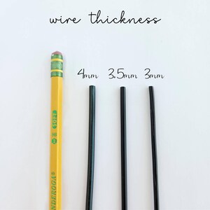 Op de afbeelding: Een gele potlood met een roze gum naast drie zwarte draden van verschillende diktes: 4 mm, 3,5 mm en 3 mm. De tekst "wire thickness" staat boven de draden. Het potlood is gemarkeerd met "ENDEROGA".