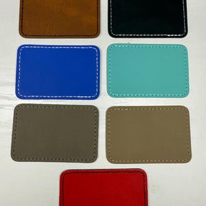 May include: A collection of rectangular patches in various colors, including brown, black, blue, teal, gray, tan, and red. Each patch has a stitched border in a contrasting color, creating a defined edge. The patches are arranged on a white surface.