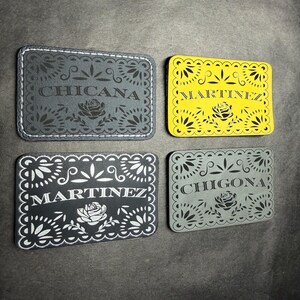 May include: Four rectangular patches with rounded corners featuring intricate floral and scalloped border designs. The patches display the text CHICANA, MARTINEZ, MARTINEZ, and CHIGONA in black or white lettering, each centered above a rose illustration.