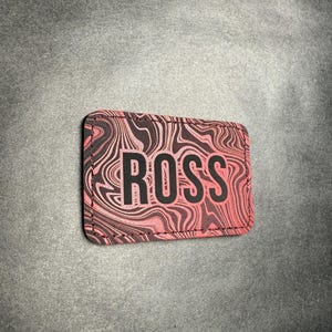 May include: A rectangular patch with the name "ROSS" in bold black letters. The patch has a pink and brown swirled pattern background and a black border.