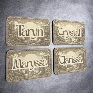 May include: Four rectangular name tags with a western theme. Each tag features a name: Taryn, Crystal, Maryssa, and Clarissa, in a serif font. The tags have a beige background with a design of cacti, cowboy boots, and a rope.