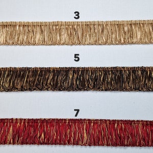May include: Three samples of gold trim fringe with different colored bases. The top sample is a light gold base, the middle sample is a dark brown base, and the bottom sample is a red base.