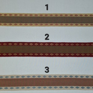 May include: Three samples of woven trim with different patterns. The first trim is beige with brown stripes and red diamond shapes. The second trim is brown with red stripes and gold diamond shapes. The third trim is beige with red stripes and blue diamond shapes.