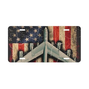 May include: License plate featuring a distressed American flag design with a B-52 bomber superimposed over it. The plate has a vintage, weathered look with red, white, and blue colors. The bomber is gray and has multiple missiles attached to its wings.