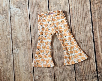 May include: White and orange pumpkin print baby pants with a flared leg. The pants are made of a soft material and are designed for comfort. The pants are a fall-themed item.