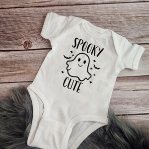 Pode incluir: Macac&atilde;o branco para beb&ecirc; com um gr&aacute;fico de fantasma preto e o texto "Spooky Cute".