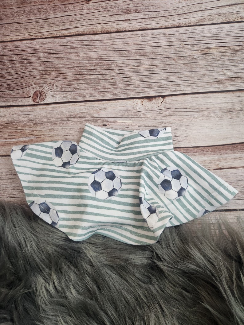 May include: A green and white striped skirt with a soccer ball pattern. The skirt has a ruffled hem and is made of a soft, comfortable fabric.