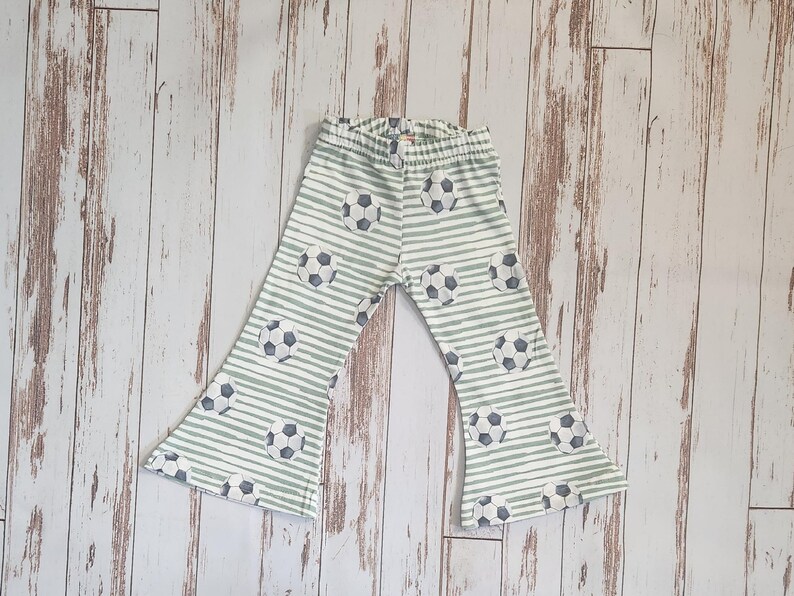 May include: White and green striped pants with a soccer ball pattern. The pants have a wide leg and a flared bottom.