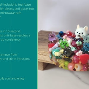 K&ouml;nnte beinhalten: Ein farbenfrohes Kunstwerk aus Harz mit verschiedenen kleinen Tierfiguren und Perlen. Das St&uuml;ck enth&auml;lt einen wei&szlig;en Hund, einen blauen B&auml;ren und andere Tierfiguren. Der Text auf der linken Seite enth&auml;lt Gebrauchsanweisungen.