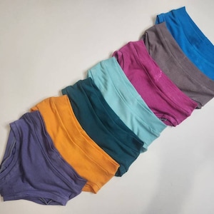 May include: A set of eight pairs of underwear in various colors, including purple, orange, teal, light blue, pink, gray, and blue.