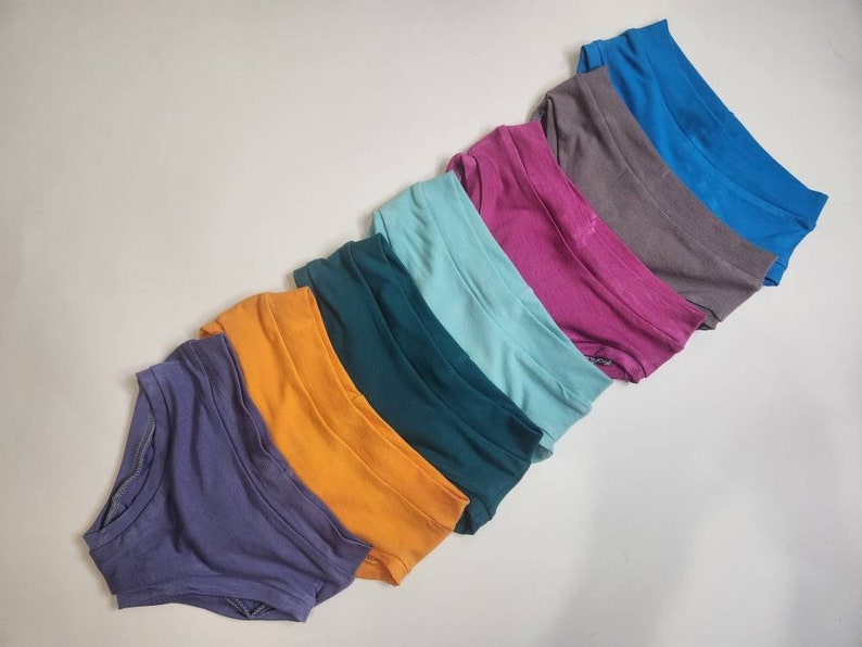May include: A set of eight pairs of underwear in various colors, including purple, orange, teal, light blue, pink, gray, and blue.