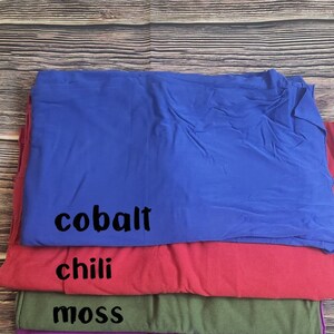 May include: Stack of four fabric swatches in different colors. The top swatch is cobalt blue, the second is chili red, the third is moss green, and the bottom is purple.