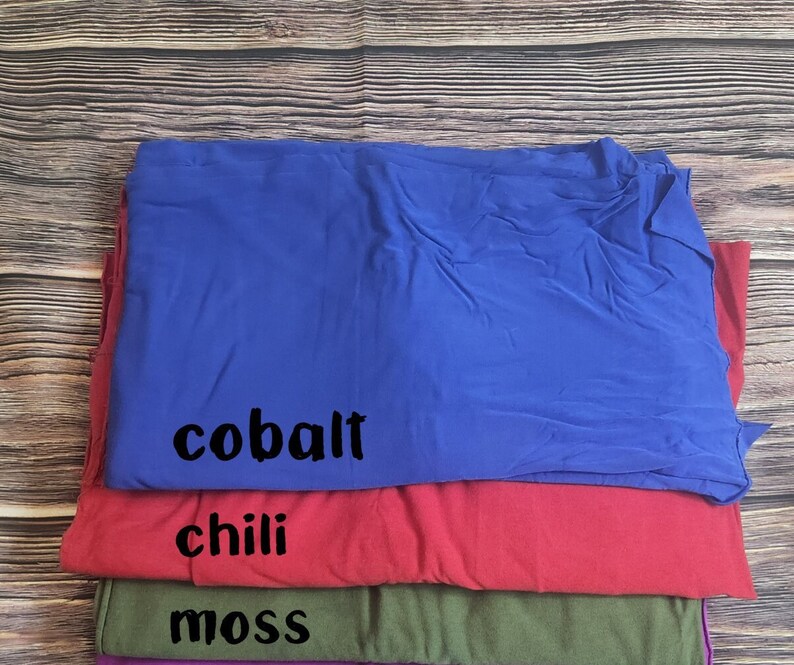May include: Stack of four fabric swatches in different colors. The top swatch is cobalt blue, the second is chili red, the third is moss green, and the bottom is purple.