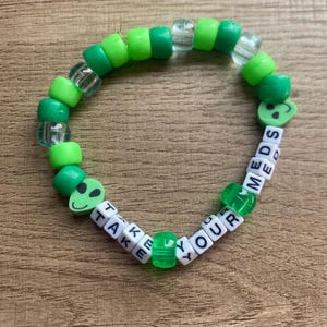 May include: Green and white beaded bracelet with the words "Take Your Meds" and alien face charms.