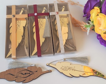 May include: Four gold feather bookmarks with Arabic calligraphy and tassels in clear boxes with brown, white, and red ribbon. Two additional bookmarks are shown, one with a wooden feather and the other with a gold feather.
