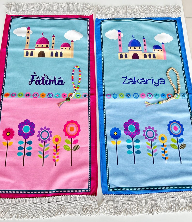 Puede incluir: Dos alfombras de oraci&oacute;n azul y rosa con dise&ntilde;os de flores coloridas y los nombres Fatima y Zakariya impresos en ellas. Cada alfombra tiene un peque&ntilde;o borla y una cuerda de cuentas.