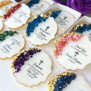 May include: White round favors with gold trim and colorful crystal accents. Each favor has a cross and text that says "Thank You for celebrating with us!"  "Sarah's Baptism"  "15.02.23"  "Godparents are a blessing thank you for being mine Alice Rose 15.02.23"  "Benjamin's Baptism Thanks for coming April 21, 2023"  "Arthur's Christening July 21, 2023"