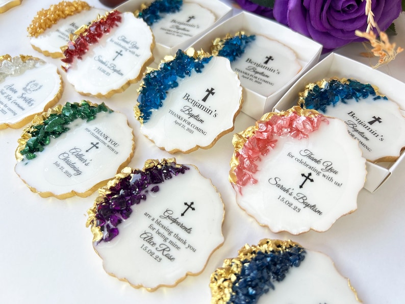 May include: White round favors with gold trim and colorful crystal accents. Each favor has a cross and text that says "Thank You for celebrating with us!"  "Sarah's Baptism"  "15.02.23"  "Godparents are a blessing thank you for being mine Alice Rose 15.02.23"  "Benjamin's Baptism Thanks for coming April 21, 2023"  "Arthur's Christening July 21, 2023"