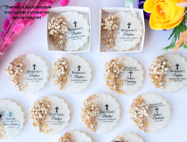 May include: White epoxy magnets with a scalloped edge, decorated with dried flowers and gold accents. Each magnet features a cross and personalized text for a baptism or christening. The magnets are packaged in white boxes.