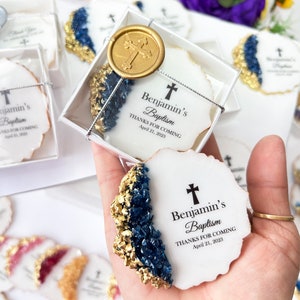 May include: White favor boxes with blue and gold accents, containing cookies decorated with a cross and the text "Benjamin's Baptism Thanks for Coming April 21, 2023".