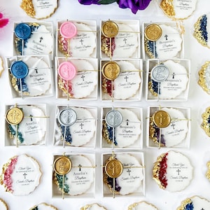 May include: Assortment of white and gold decorated cookies with various wax seals in a variety of colors. The cookies are packaged in clear boxes with white lids. The cookies have text that reads "Thank you for celebrating with us at Sarah's Baptism" and "Benjamin's Baptism".