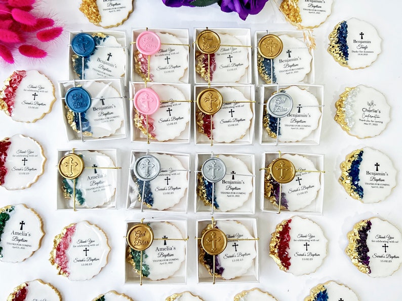 May include: Assortment of white and gold decorated cookies with various wax seals in a variety of colors. The cookies are packaged in clear boxes with white lids. The cookies have text that reads "Thank you for celebrating with us at Sarah's Baptism" and "Benjamin's Baptism".