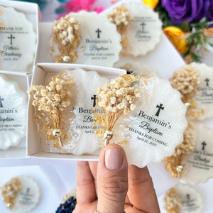 May include: White and gold resin coasters with dried floral accents. Each coaster features a cross and the text "Benjamin's Baptism" and "Thanks for coming April 21, 2023". Some coasters are in a white box.