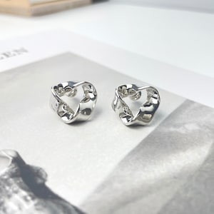 Könnte beinhalten: Ein Paar silberne Ohrringe mit einem gedrehten, offenen Design. Die Ohrringe sind aus glattem, glänzendem Metall.