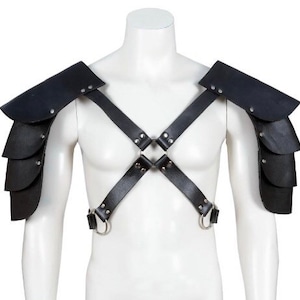 May include: Black leather shoulder armour with layered plates and riveted details. The armour features a harness design with adjustable straps and metal rings, displayed on a mannequin.