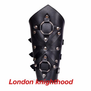May include: Black leather arm guard with metal rings and rivets. The arm guard has a pointed top and is secured with straps and buckles. The text "London knighthood" is printed at the bottom.