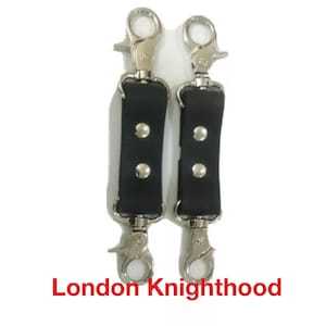 May include: Two black leather straps with silver metal clasps and three silver metal studs on each strap. The straps are labelled "London Knighthood".