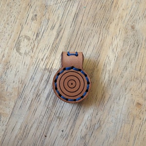 May include: A brown leather key chain with a blue stitched circle design.