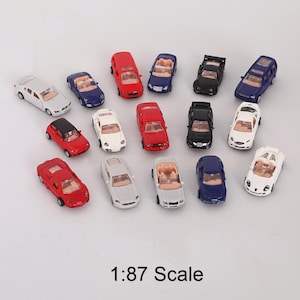 May include: A collection of miniature toy cars in various colors, including red, white, black, and blue. The cars are a 1:87 scale, with convertible and sedan styles visible. The image shows a variety of car models.