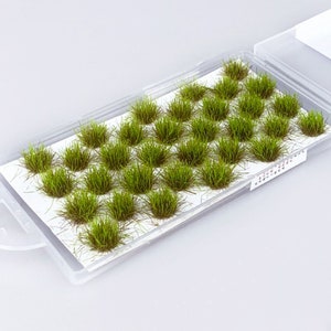 Op de afbeelding: Een transparante plastic container gevuld met 36 kleine, groene plukjes kunstgras. De container is ontworpen voor modeltreinen of miniatuurlandschapsarchitectuur.