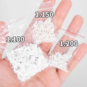 Könnte beinhalten: Drei Beutel mit weißen Plastikfiguren in verschiedenen Größen. Die Beutel sind mit 1:100, 1:150 und 1:200 beschriftet.