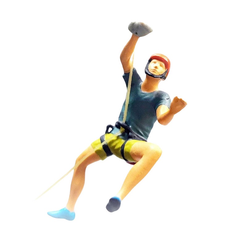 May include: A figurine of a rock climber wearing a red helmet, blue shorts, and a blue shirt, holding onto a rock with a rope attached to their waist.