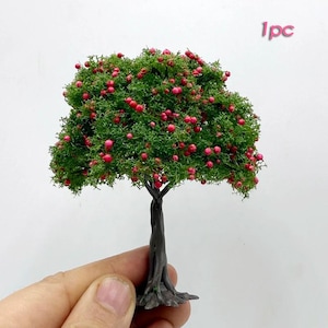 Peut inclure: Petit arbre miniature avec un tronc brun foncé et un feuillage vert touffu parsemé de petites baies rouges. L'arbre est tenu dans une main sur fond blanc. Le texte "1pc" est visible.