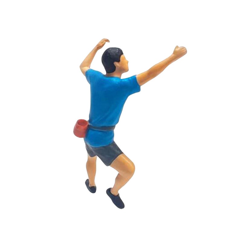 May include: A blue and black figurine of a person rock climbing. The figurine is wearing a blue shirt, black shorts, and a red climbing harness.