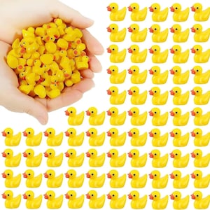 May include: A collection of small, yellow rubber duck figurines with orange beaks and black eyes. Some ducks are held in a hand, while others are arranged in neat rows. The ducks are a bright yellow color.