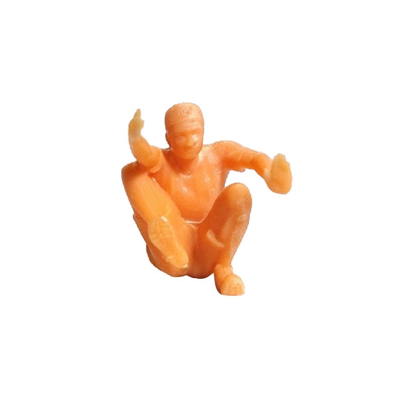 May include: A small, orange plastic figurine of a person sitting with their legs crossed and arms outstretched.