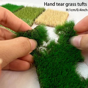 May include: Hand tear grass tufts with a height of 0.4 inches. The product consists of rectangular patches of artificial grass in shades of vibrant green and dried tan, featuring a textured, fibrous surface for miniature modeling projects.