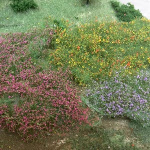 Op de afbeelding: Een miniatuurlandschap met kleurrijke bloemen en groen. De scène bevat levendige roze, gele en paarse bloemen afgewisseld met groen gras, waardoor een textuurrijke en visueel aantrekkelijke weergave ontstaat.