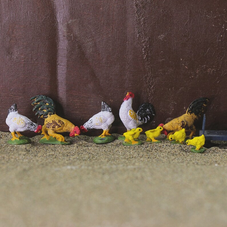 May include: A set of toy farm animals, including a white rooster, a yellow hen, and several yellow chicks. The animals are made of plastic and have a realistic appearance.