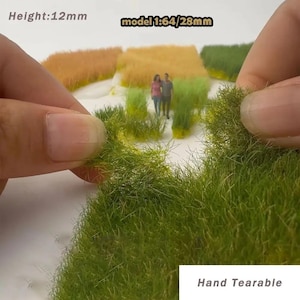 May include: Close-up of green model grass, held by a hand, with a height of 12mm. The image also shows miniature figures of a couple and patches of model fields in various colors. The text "Hand Tearable" is visible.