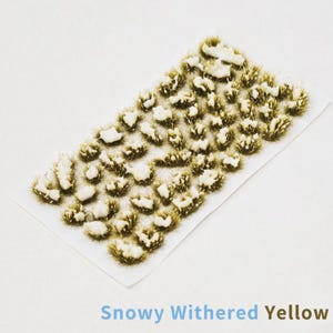 Może przedstawiać: Arkusz miniaturowej scenerii modelarskiej z kępami zwiędłej żółtej trawy z płatami białego śniegu. Tekst "Snowy Withered Yellow" jest wydrukowany na niebiesko na dole. Idealny do makiet kolejowych i dioram.
