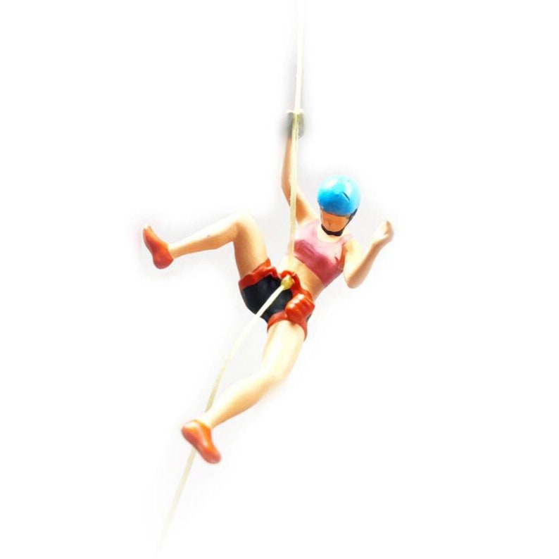 May include: A figurine of a person abseiling down a rope, wearing a blue helmet, pink sports bra, black shorts, and red climbing gear.