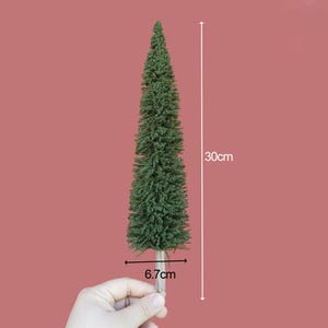 Könnte beinhalten: Ein grünes künstliches Kiefernbaummodell, 30 cm hoch und 6,7 cm breit, mit einem braunen Holzsockel.